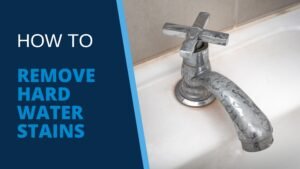 Silver tub faucet, stained white with hard water mineral deposits, sits on white tub with grey tiles on bathroom wall behind, illustrating blog post “How to Remove Hard Water Stains”